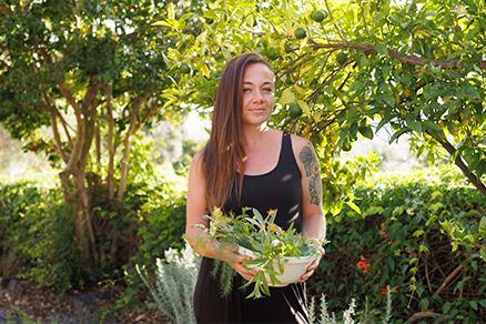 Woman holding edible flowers in bowl by tree